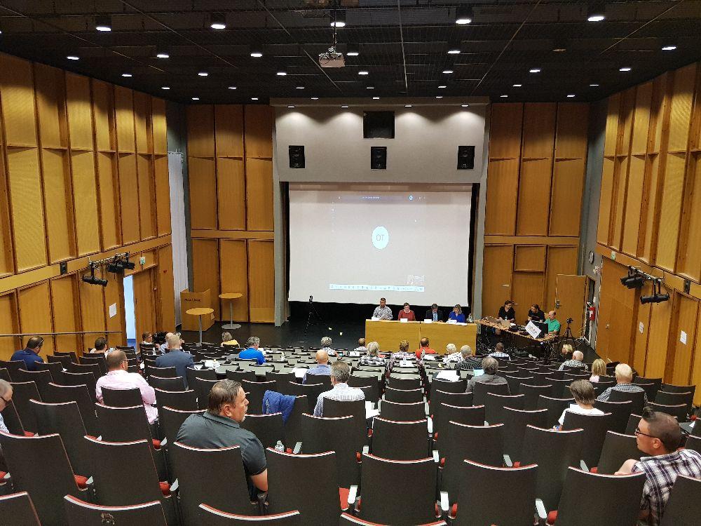 Auditorium med ledamöter långt från varandra. LÄngst ner syns ordförande, sekreterare etc, plus ett videoinspelningsteam.