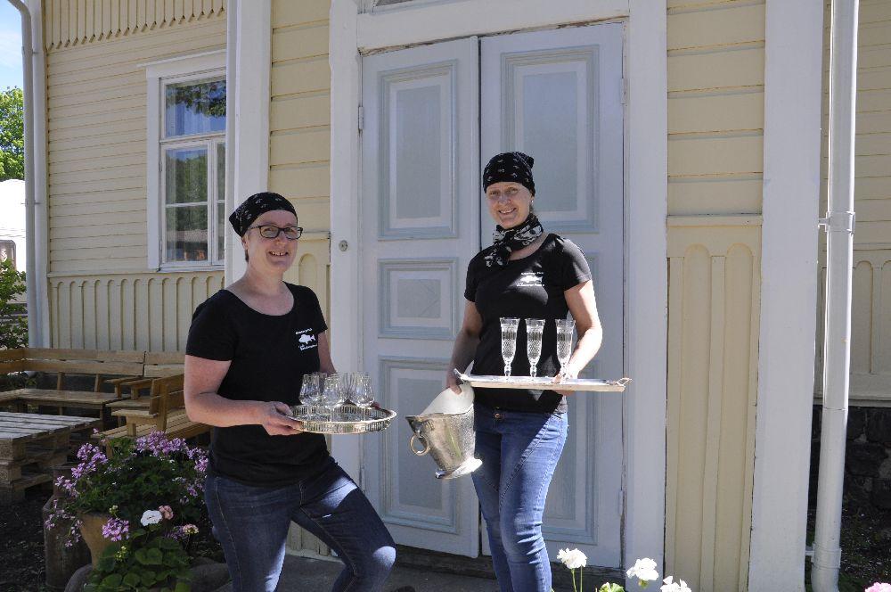 Två damer vid en nymålad dörr. I händerna har de glas och brickor.