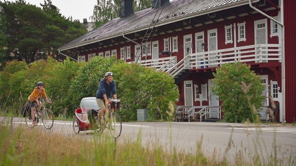Två cyklister åker förbi ett rött loftgångshus