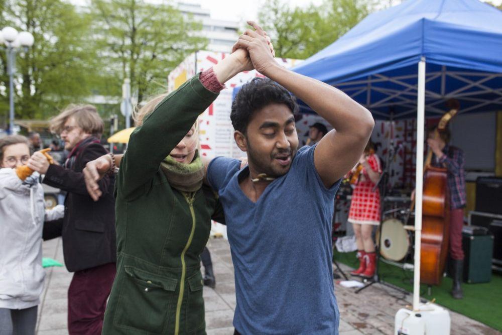 En kvinna och en man klädda i ytterkläder dansar med varandra utomhus framför ett tält där ett band spelar..